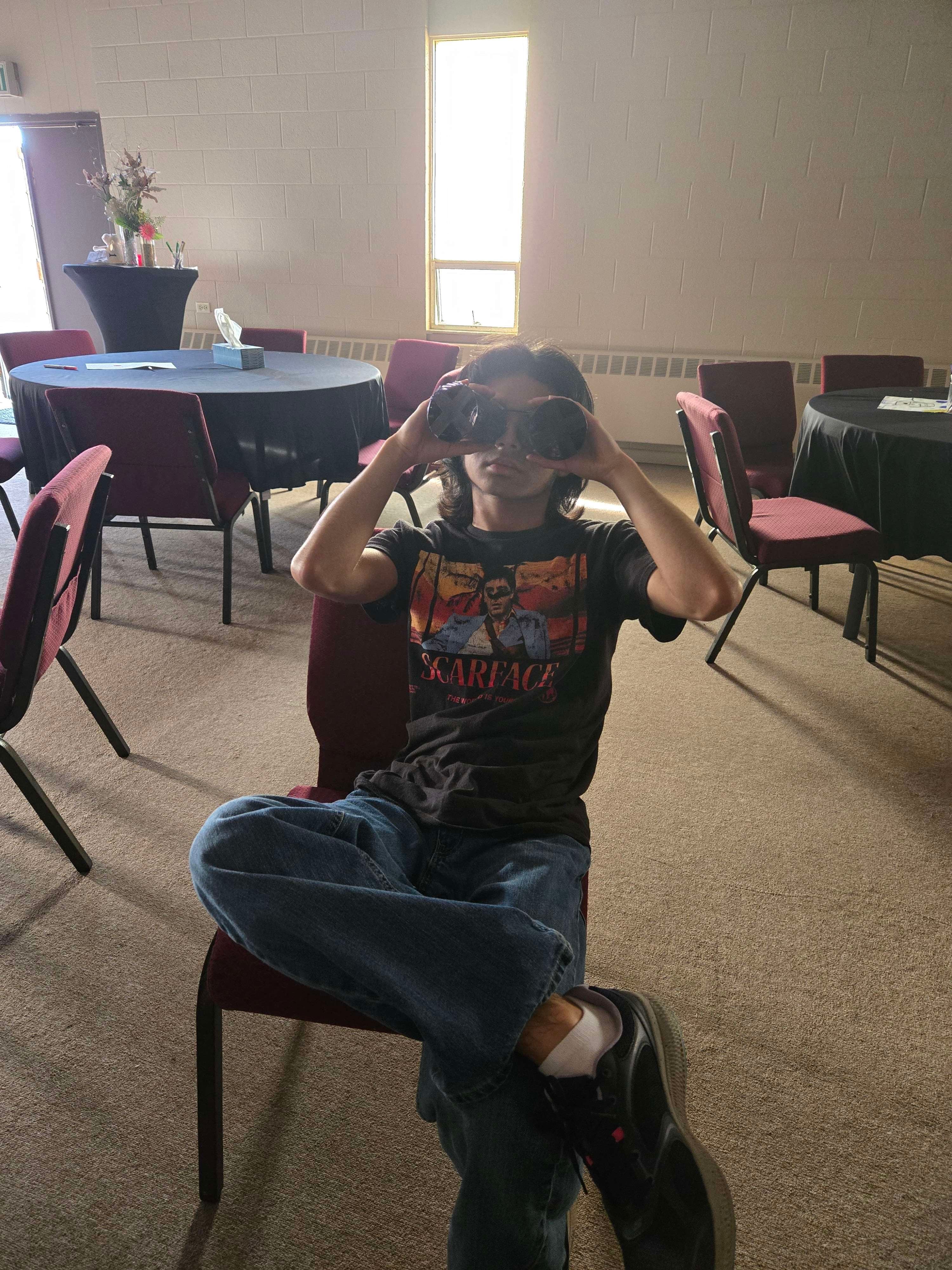 youth holding up paper towel rolls as binoculars sitting in a chair